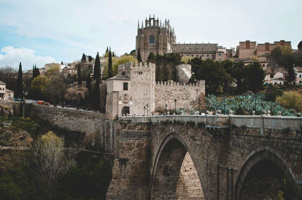 Majestic view of a medieval bridge and castle in Toledo, Spain, with lush green surroundings.